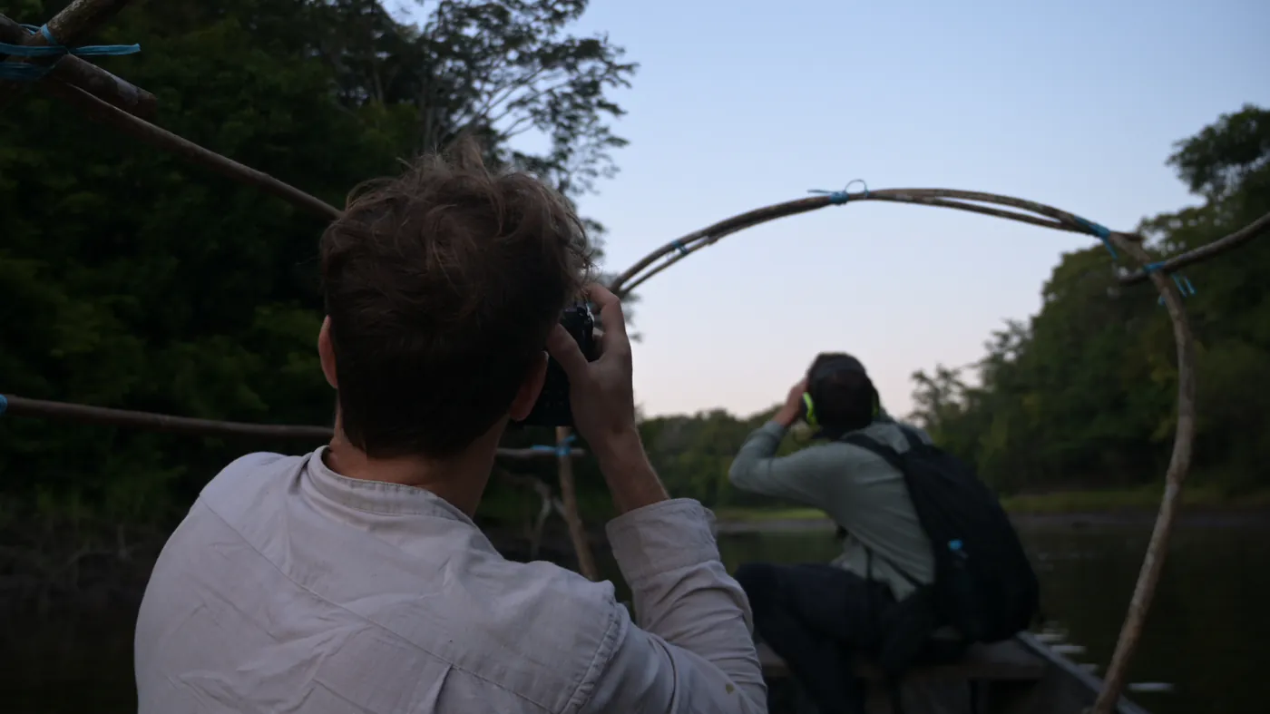 Deux photographes guettent la rive depuis un bateau, au crépuscule.