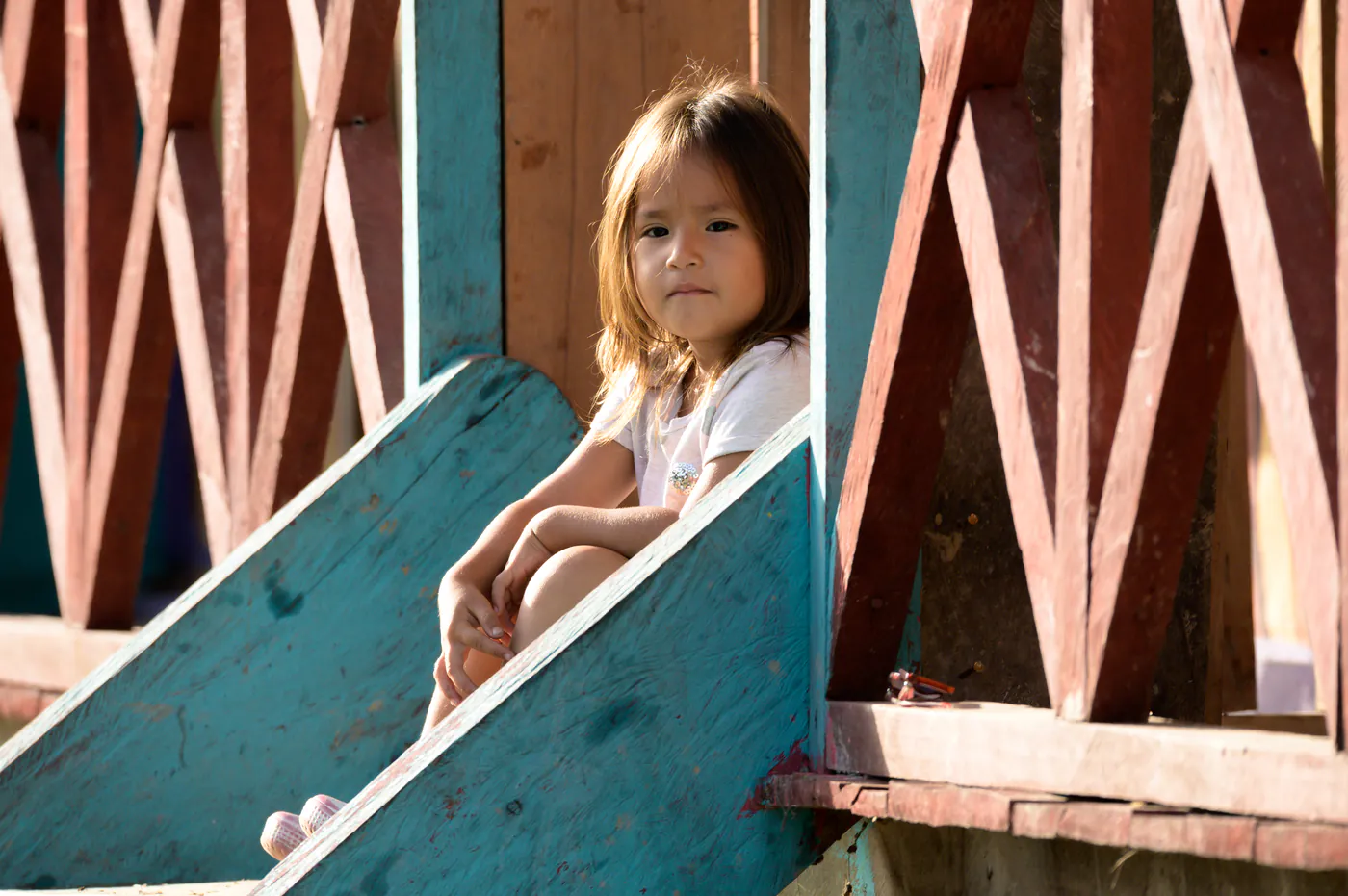 Une petite fille assise dans un escalier de bois peint en bleu.