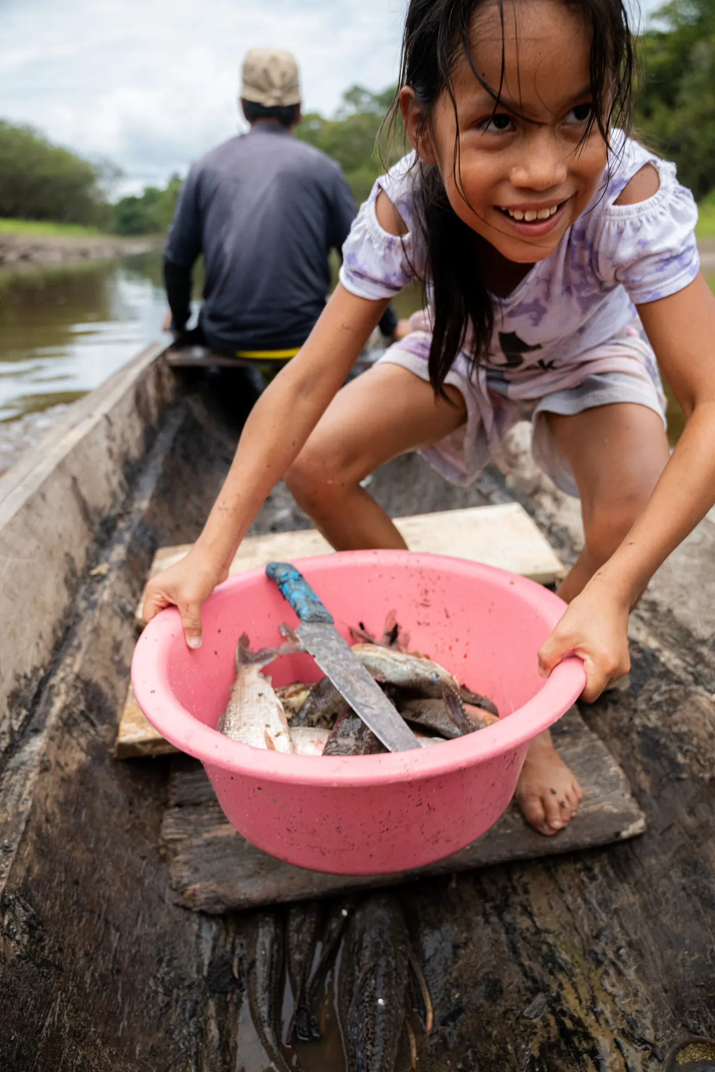 Une fillette sourit, accroupie dans une pirogue, tenant une bassine de poissons.