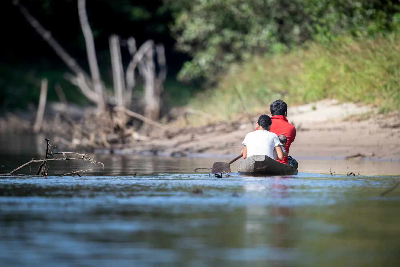 Deux personnes en pirogue remontent la rivière, à contre-jour.