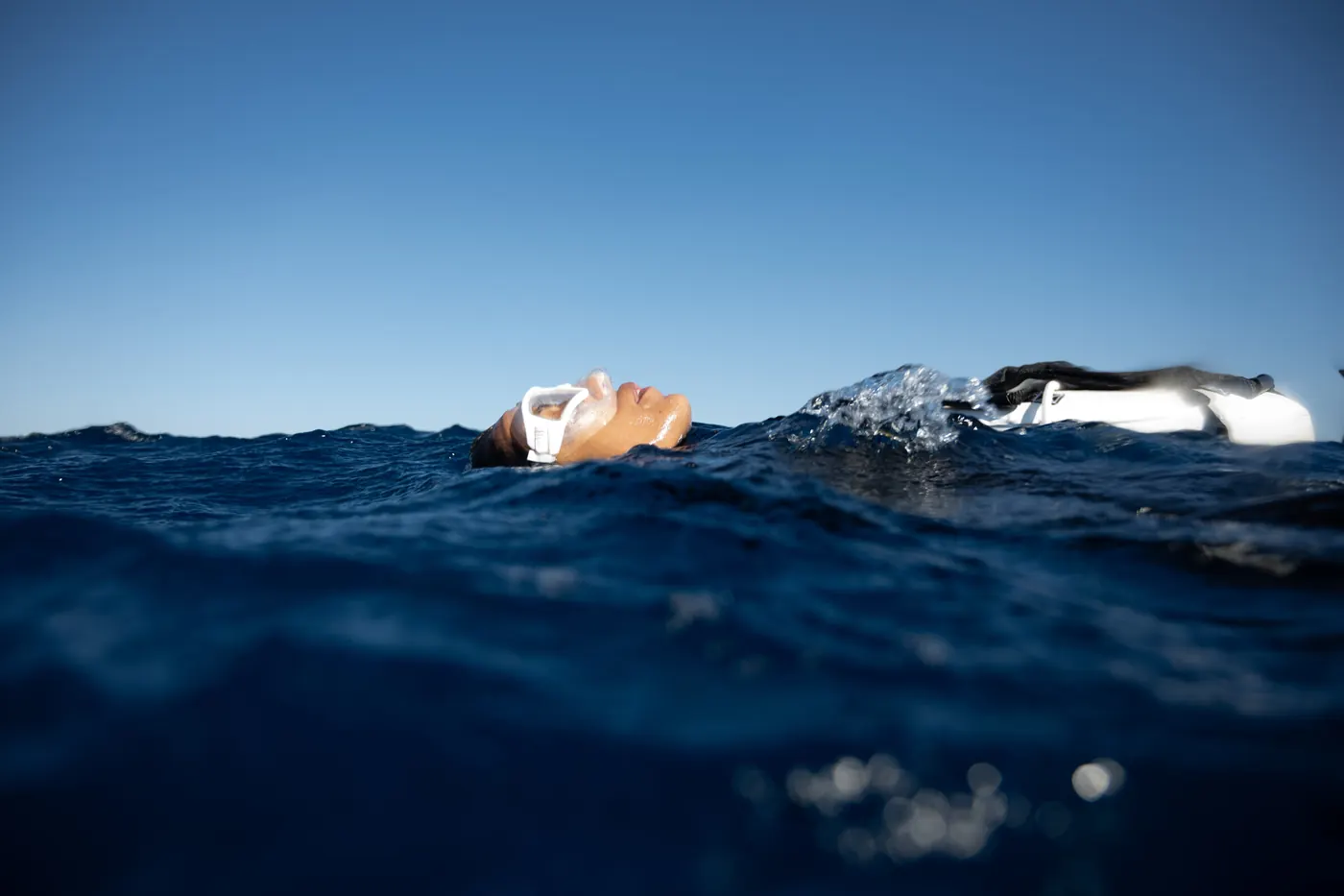 Une apnéiste allongée à la surface, photographiée au ras de l’eau : le ciel en haut, la mer sombre en bas.